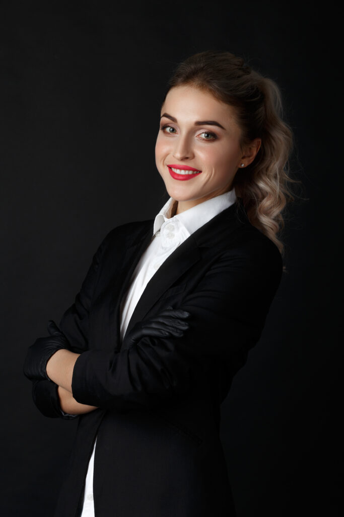 smart blonde with long curly hair poses in black jacket and black gloves in a dark studio